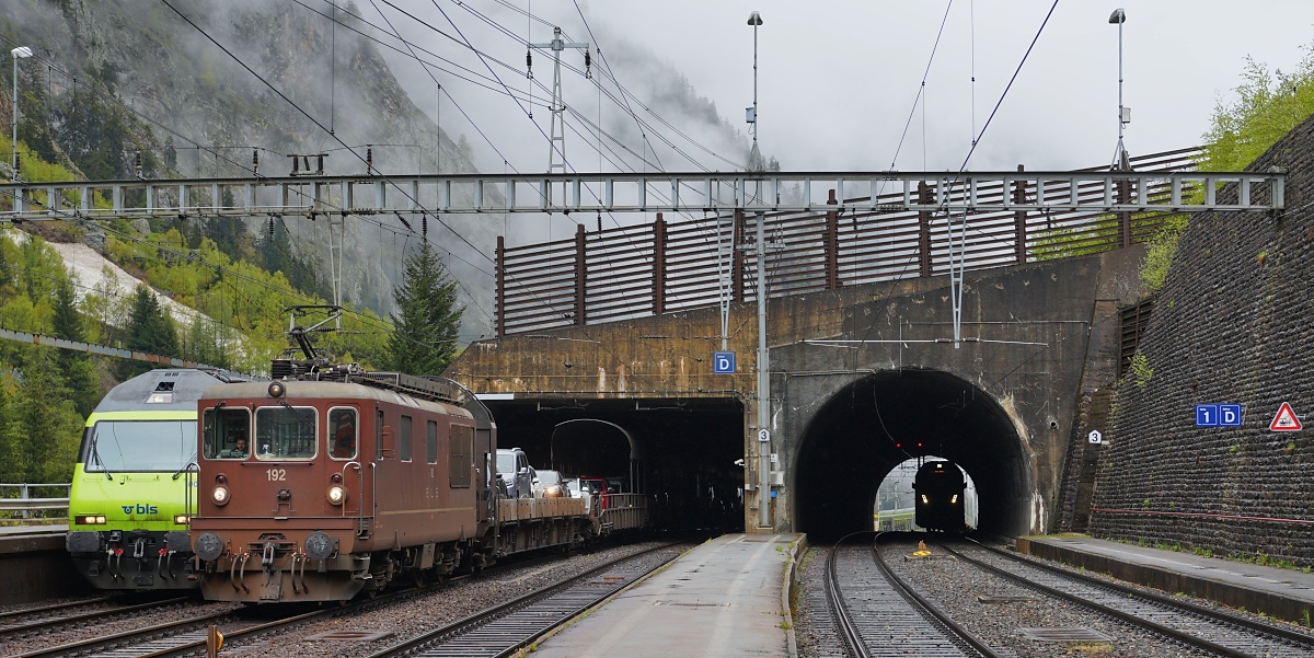 Am 07.05.2024 warten die Re 465 002 und Re 425 192 im Bahnhof Goppenstein vor ihren Autozügen auf die Abfahrt durch den Lötschbergtunnel nach Kandersteg, rechts im Tunnel nähert sich der RABe 528 112