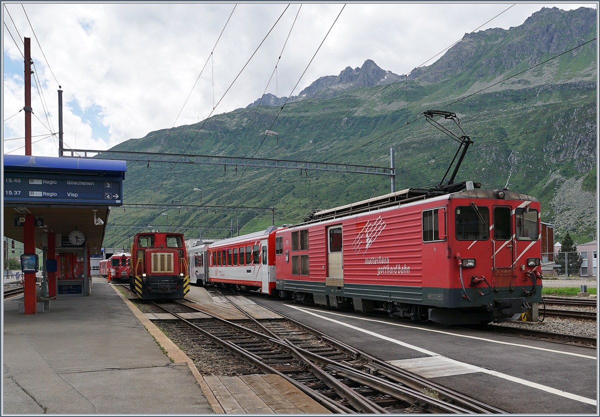 Da auf der steilen Sch�llenen Bahn die Anh�ngelast begrenzt ist, werden jeweils in Andermatt die von Visp kommenden Verst�rkungswagen abgeh�ngt und dann gleich dem Gegenzug �bergeben. Hier holt die  Sch�ma  Disellok nach der Ausfahrt des Zuges nach G�schenen die Wagen ab, w�hrend rechts der BDeh 4/4 54 (mit seinem Regionalzug nach Visp) f�r das Ankuppeln der Verst�rkungswagen bereit steht.
28. Juli 2016