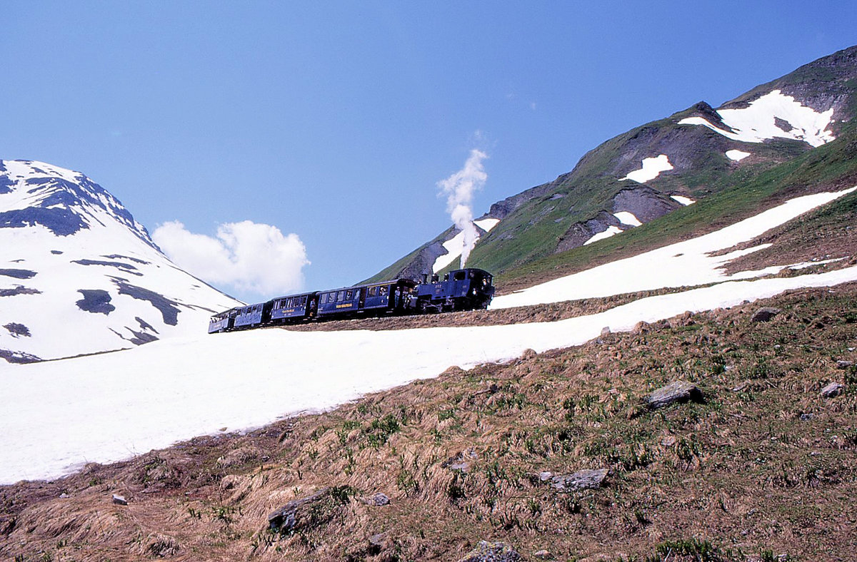 Dampfbahn Furka Bergstrecke: Im Juli liegen noch grosse Schneemengen auf der Strecke - entsprechend musste die FO früher den Betrieb Oberwald - Realp im Winter einstellen. Hier kommt Lok 2 mit ihrem Zug von der Furka herunter. Die Lok fuhr damals rückwärts ins Tal; heute fährt sie vorwärts. 1.Juli 1995 