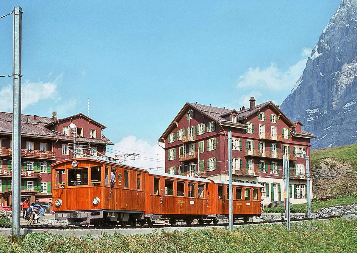 Jungfraubahn Lok 11 mit ihren Wagen 17 und 18 auf der Kleinen Scheidegg, 5.August 1975. Lok 11 wurde als Zahnrad- und Adhäsionslok HGe2/2 1914 gebaut und zuerst an der Landesausstellung in Bern gezeigt. Sie blieb danach unter Pfandverschluss remisiert bis zur Inbetriebnahme 1924. 1952 wurde sie zur reinen Zahnradlok He2/2 umgebaut. 1966 wurde der Kasten abgebrochen, und seither trägt die  neue  Lok 11 den Kasten der ehemaligen Lok 12. Seit 2017 ist die Lok Denkmal in Interlaken. Von den beiden 1912 gebauten Wagen wurde Nr. 17 1994 als  Eiger Ambassador Express  hergerichtet; seit 2017 ist er - soviel ich weiss - in Zweilütschinen remisiert. Wagen 18 wurde 2001 abgebrochen.    