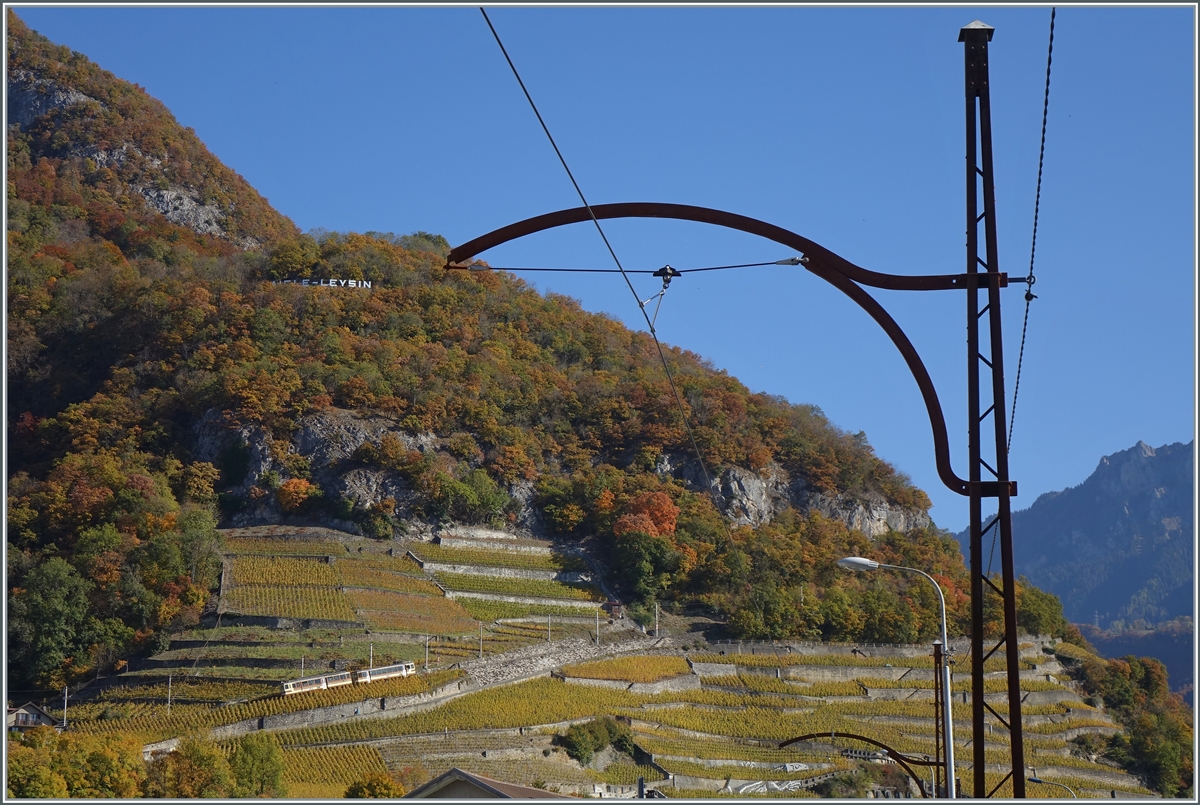 Vom alten Fahrleitungsmast der ASD eingerahmt, schiebt der A-L BDeh 4/4 kurz nach Aigle seinen Bt durch die Weinberge in Zug in Richtung Leysin. Da hier die ASD im Strassenbereich verläuft befindet sich die  Fotostelle  ebenfalls auf der Strasse. 27. Oktober 2021