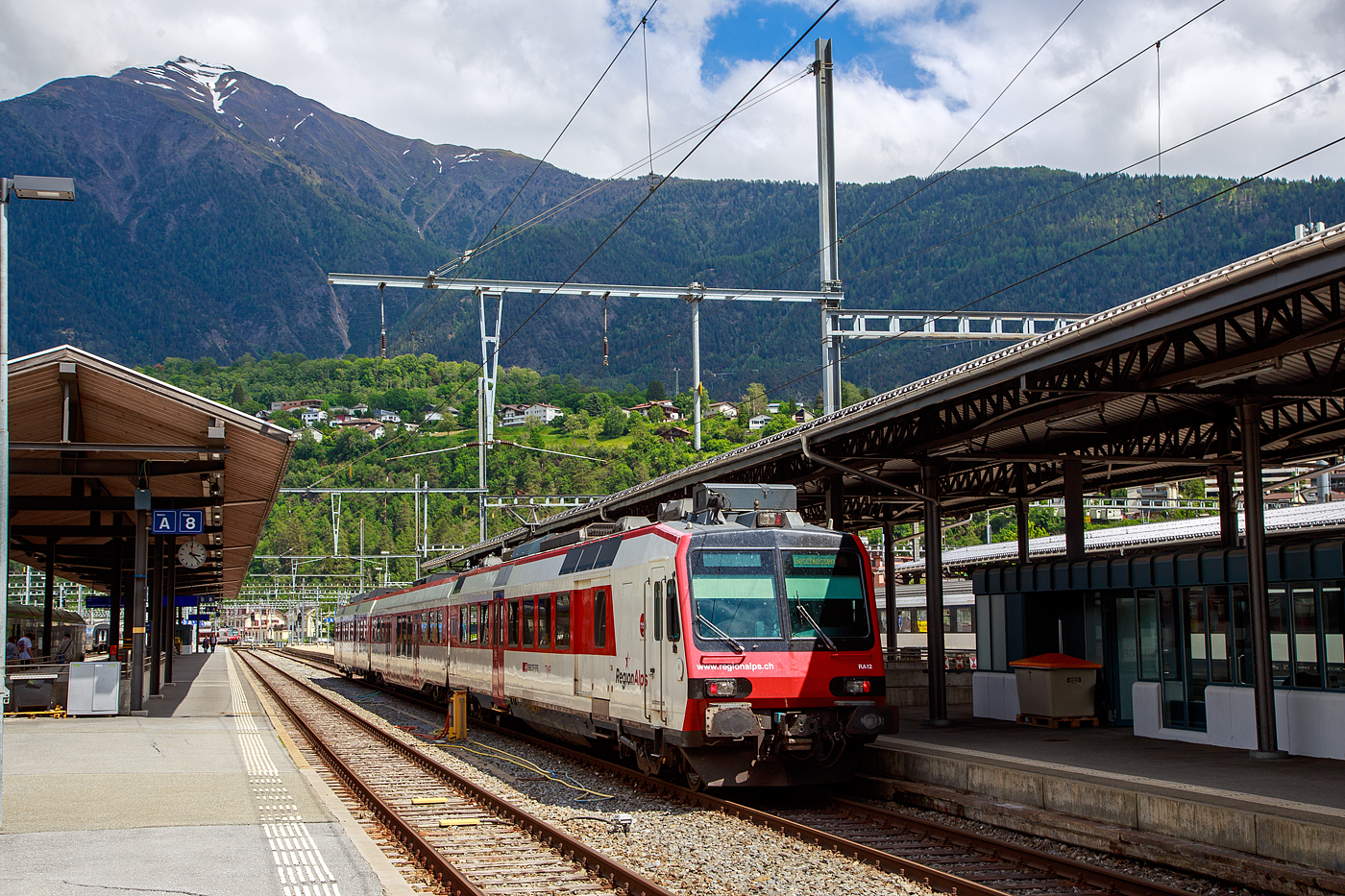 Der dreiteilige NPZ Domino RA12 der RegionAlps (ex SBB RBDe 4/4) hat am 25.05.2023 als Regio (St-Gingolph–St-Maurice –Martigny–Sion–Brig), Steuerwagen voraus, seinen Zielbahnhof Brig erreicht.

Der NPZ Domino besteht aus:
1./2. Klasse Steuerwagen ABt NPZ DO RA 50 85 39-43 948-1 CH-RA
Modernen 2.Klasse INOVA-Zwischenwagen mit Niederfluranteil B NPZ DO RA 50 85 29-43 407-0 CH-RA
und dem 
Triebwagen RBDe 560 DO RA 94 85 7 560 412-9 CH-RA, ex SBB RBDe 560 010-1 (Umbau 2009), hier rechts im Vordergrund.

Die Regionalps (RA) ist ein Eisenbahnverkehrsunternehmen im Kanton Wallis, mit Sitz in Martigny hat. Eigentümer derim Jahr 2003 gegründete Gesellschaft  sind die Schweizerischen Bundesbahnen (SBB) mit 70 %, die Transports de Martigny et Régions (TMR) mit 18 % und der Kanton Wallis mit 12 %. Die RA betreibt den Regionalverkehr vor allem im Rhonetal zwischen dem Ostufer des Genfersees und Brig. Inzwischen gehören Regionalps 16 dreiteilige NPZ Domino (Trieb-, Zwischen- und Steuerwagen ex SBB) und 4 RABe 525 NINA (ex TMR).

Als RBDe 4/4 wurden die Triebwagen der Schweizerischen Bundesbahnen (SBB) bezeichnet, die ab 1984 für die als Neuer Pendelzug (NPZ) bezeichneten Regionalzugskompositionen mit den dazugehörenden Steuerwagen angeschafft wurden. Sie tragen seit 1990 die Baureihenbezeichnung RBDe 560. Aus Kostengründen wurde damals auf die Beschaffung neuer Zwischenwagen verzichtet, verwendet werden stattdessen umgebaute Einheitswagen (EW I und EW II).

Die meisten von 1987 bis 1996 gebauten Fahrzeuge RBDe 560, 561 und 568 durchliefen 2008 bis 2013 ein Komplett-Modernisierungsprogramm. Aus aufgearbeiteten Trieb- und Steuerwagen sowie neu beschafften Zwischenwagen entstanden Regionalverkehrs-Kompositionen mit der Bezeichnung «Domino». Die Triebwagen werden dabei einheitlich als RBDe 560 (94 85 7 560 XXX-X) bezeichnet. Sie können in Vielfachsteuerung verkehren.

TECHNISCHE DATEN (Komposition RBDe 560, B und ABt) :
Spurweite:  1.435 mm (Normalspur)
Achsformel:  Bo’Bo’ +2´2´+2´2´
Länge über Puffer:  25.000 mm / 24.700 mm / 25.000 mm
Drehzapfenabstand: 17.600 mm / 18.900 mm /17.600 mm
Achsabstand im Drehgestell: 2.700 mm (ZW 2.500 mm)
Treib- und Laufraddurchmesser: 950 mm
Höhe:  3.750 mm
Breite:  2.860 mm
Dienstgewicht:  72 t (Triebwagen) + 36 t (ZW) + 38 t (Steuerwagen)
Höchstgeschwindigkeit: 140 km/h
Dauerleistung:  1.650 kW (2.250 PS)
Anfahrzugkraft:  182 kN
Dauerzugkraft: 78 kN
Anzahl Fahrmotoren: 4
Stromsystem:  Wechselstrom 15 kV 16,7 Hz
Sitzplätze: 54 (TW) / 60 (ZW) / 12+60 (SW) = 186 (12 in der 1. Klasse)
Ladegewicht: 0,3 t (Triebwagen)
Kupplungstyp: Schraubenkupplung
