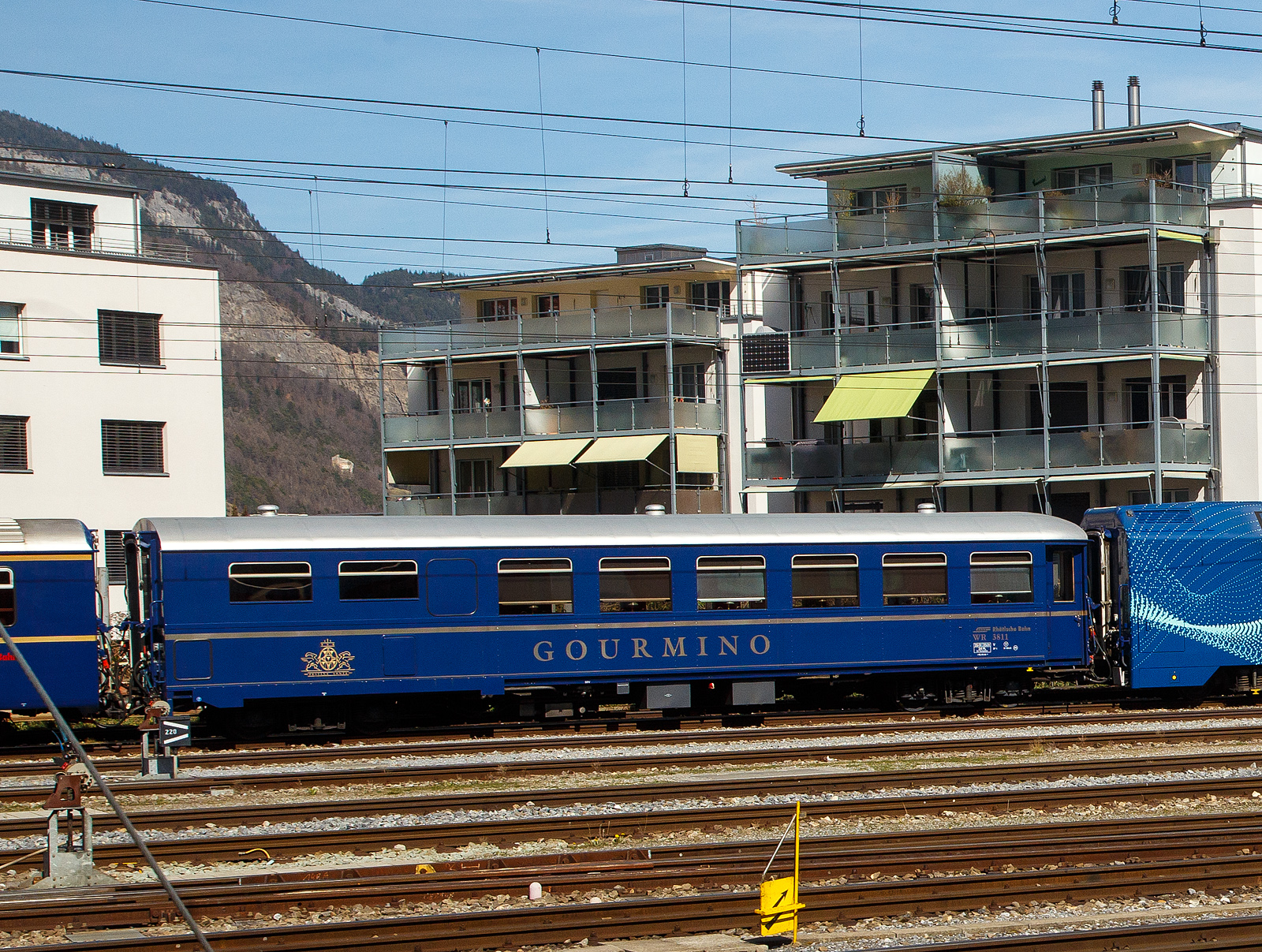 Der RhB Gourmino Speisewagen WR 3811, ex RhB Dr4ü 3811, ex Mitropa Dr4ü 11, am 22.03.2023 beim Bahnhof Chur abgestellt.

In den Jahren 1929 und 1930 beschaffte die Mitropa drei als Dr4ü 10-12 bezeichnete Speisewagen für den Einsatz in den Luxuszügen der Rhätischen Bahn. Diese Fahrzeuge liefen nicht nur im Glacier Express, sondern auch im Engadin Express und auf Verbindungen nach Davos. Lieferant war die Schweizerische Waggons- und Aufzügefabrik Schlieren (SWS). 1949 ersteigerte die RhB die Speisewagen von der Mitropa.
Die Bezeichnung Dr4ü 10-12 wurde 1956 in Dr4ü 3810-3812 und später in WR 3810-3812 geändert.

WR 3812 wurde 1974 versuchsweise modernisiert und mit Mikrowellenherden ausgerüstet. WR 3810-3811 hingegen wurden 1982 bzw. 1983 als nostalgische Speisewagen hergerichtet und mit einer neuen Kücheneinrichtung versehen, die eine Zubereitung frischer Speisen gestattet.

1996 wurde WR 3812 generalüberholt, wobei die RhB auch die Inneneinrichtung weitgehend in den Originalzustand zurückversetzte. Bei dieser Gelegenheit tauschte der Wagen sein rotes gegen ein königsblaues Farbkleid mit großem  Gourmino -Schriftzug ein. Diesen auffälligen Farbton erhielten später ebenfalls WR 3810-3811. Alle drei Wagen wurden inzwischen erneut umlackiert und präsentieren sich heute im noblen Blauton des Alpine Classic Pullman Express (ACPE). Der Gourmino fährt meist auf der spektakulären Albulalinie zwischen Chur und St. Moritz.

TECHNISCHE DATEN:
Baujahr und Hersteller: 1929 / SWS
Spurweite: 1.000 mm
Anzahl der Achsen: 4
Länge über Puffer: 16.440 mm
Sitzplätze: 36
Eigengewicht: 25,0 t
zulässige Geschwindigkeit: 90 km/h
Lauffähig: StN (Stammnetz) / MGB (Matterhorn Gotthard Bahn)
