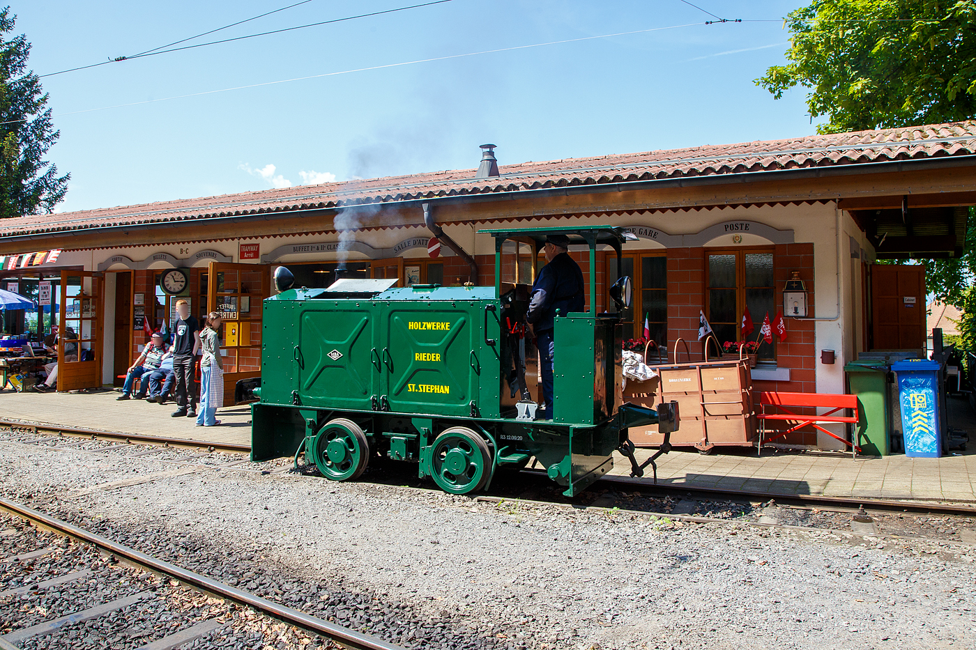 Die doch recht kleine ex MOB Schienentraktor Tm 2/2 Nr. 1, ex Holzwerk Rieder, der Museumsbahn Blonay-Chamby rangiert am 27.05.2023 im Museumsareal in Chaulin. 

Die kleine Diesellok, vom Typ O&K RL 2a wurde 1931 von Orenstein & Koppel im Werk Babelsberg unter der Fabriknummer 20200 gebaut und an die Grande Dixence SA für die Baustelle der ersten Dixence-Staumauer  geliefert, wo sie bis 1940 im Einsatz war. Im 1941 wurde sie dann von der Firma Mauerhofer & Zubner, für den Einsatz von Bauzügen beim Fahrleitungsumbau bei der MOB übernommen. 1950 wurde die kleine Lok an das Holzwerk Rieder in St. Stephan verkauft, diese Farbgebung trägt sie auch aktuell bei der BC. Die Lok trägt Fabrikschilder der MBA, wobei die Umbenennung der O&K in Maschinenbau und Bahnbedarf Aktiengesellschaft, vormals Orenstein & Koppel (MBA) erst im Februar 1940 erfolgte.

Die MOB (Montreux-Berner Oberland-Bahn / Montreux Oberland Bernois) kaufte die Lok dann 1979 wieder zurück und bezeichnete sie als Tm 2/2 1. Bei der MOB wurde sie für Rangierarbeiten, von Zementwagen auf Rollböcken in St. Stephan eingesetzt. Die Lok wurde 1995 von der MOB ausrangiert verbleib aber erst noch im Depot Montbovon. 2006 ging sie dann an die Museumsbahn Blonay-Chamby.

Die Lok hat einen 2-Zylinder-Orenstein & Koppel-Dieselmotor mit 22 PS (16 kW) Leistung, die Leistungsübertragung erfolgt über ein Zweigang-Konuskupplungs-Wendegetriebe mit stufenloser Geschwindigkeit Regulierung, über zwei Rollenketten auf die vordere Achse und von dieser über eine Rollenkette auf die hintere Achse. Das Zweigang-Konuskupplungsgetriebe ermöglicht zwei verschiedene Geschwindigkeitsstufen für beide Fahrtrichtungen. Dabei laufen immer beide Gänge im Eingriff, jeweils einer wird eingekuppelt. Eine einfache Wendeschaltung im Getriebe ermöglicht den Fahrtrichtungswechsel bei Stillstand der Lokomotive. Die einfache Bauart des Getriebes hat sich schon bei den Benzinloks bewährt und wurde bei fast allen O&K-Loks der unteren Leistungsklassen angewendet.

TECHNISCHE DATEN:
Spurweite: 1.000 mm (Meterspur)
Achsfolge: B
Länge über Puffer: 4.490 mm
Kastenlänge: 3.450 mm
Höhe: 2.270 mm
Breite: 1.240 mm
Achsabstand: 1.170 mm
Raddurchmesser : 550 mm
Eigengewicht: 7.000 kg
Leistung: 16 kW (22 PS)
Höchstgeschwindigkeit: 7 km/h
Achslager: Gleitlager

Die O&K Typenbezeichnung  RL  stand für  Rohöl  (= Diesel).

Anfang des 20. Jahrhunderts war es noch üblich bei und auf Großbaustellen Feld- oder Schmalspurbahnen zu bauen und zu betreiben. Heute durch Entwicklung von moderner und oft sehr schweren Baumaschinen und Muldenkipper eigentlich undenkbar.