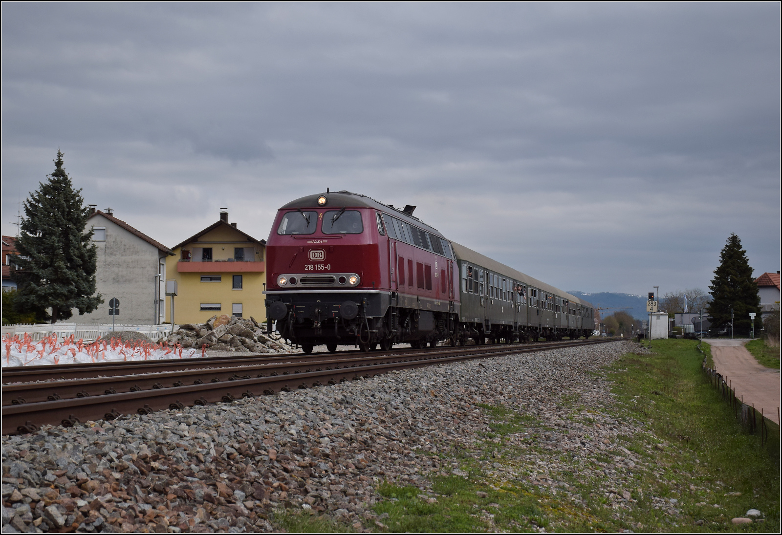 Dieselabschiedsfahrt am Hochrhein. 

218 155 fährt zum zweiten Mal mit vielen geneigten Fahrgästen im Zug der EFZ nach Basel. Die Lok wie aus der Märklinschachtel, den Hotzenwald im Rücken geht es hier durch die Baustelle für den neuen Haltepunkt Warmbach. März 2026.