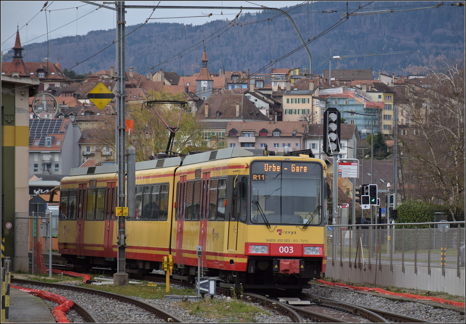 Ende einer Ära.

Die Gleichstromära in Orbe neigt sich dem Ende zu, während sich die Karlsruher Zweisystem-Strassenbahn  Be 4/8 003  alias 94 800 450 003-9 D-TVYS in die Kurve neigt, um in das letzte stark ansteigende Teilstück einzubiegen. Im Hintergrund das zu Zeiten des Streckenbaus der Schweizer Bahnen links liegen gebliebene Städtchen Orbe. Dezember 2025.