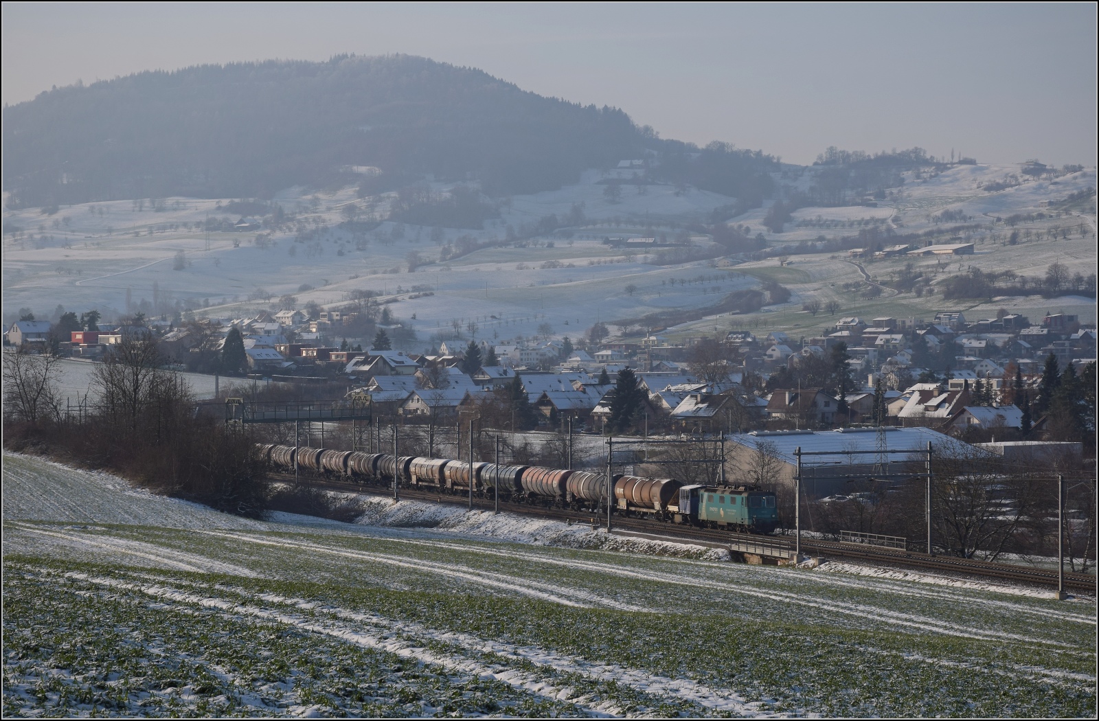 Re 430 114 von WRS mit Synopsis-Werbung schleppt die Rangierhilfe Tm III 9530 mit über den Bözberg. Frick, Dezember 2022.
