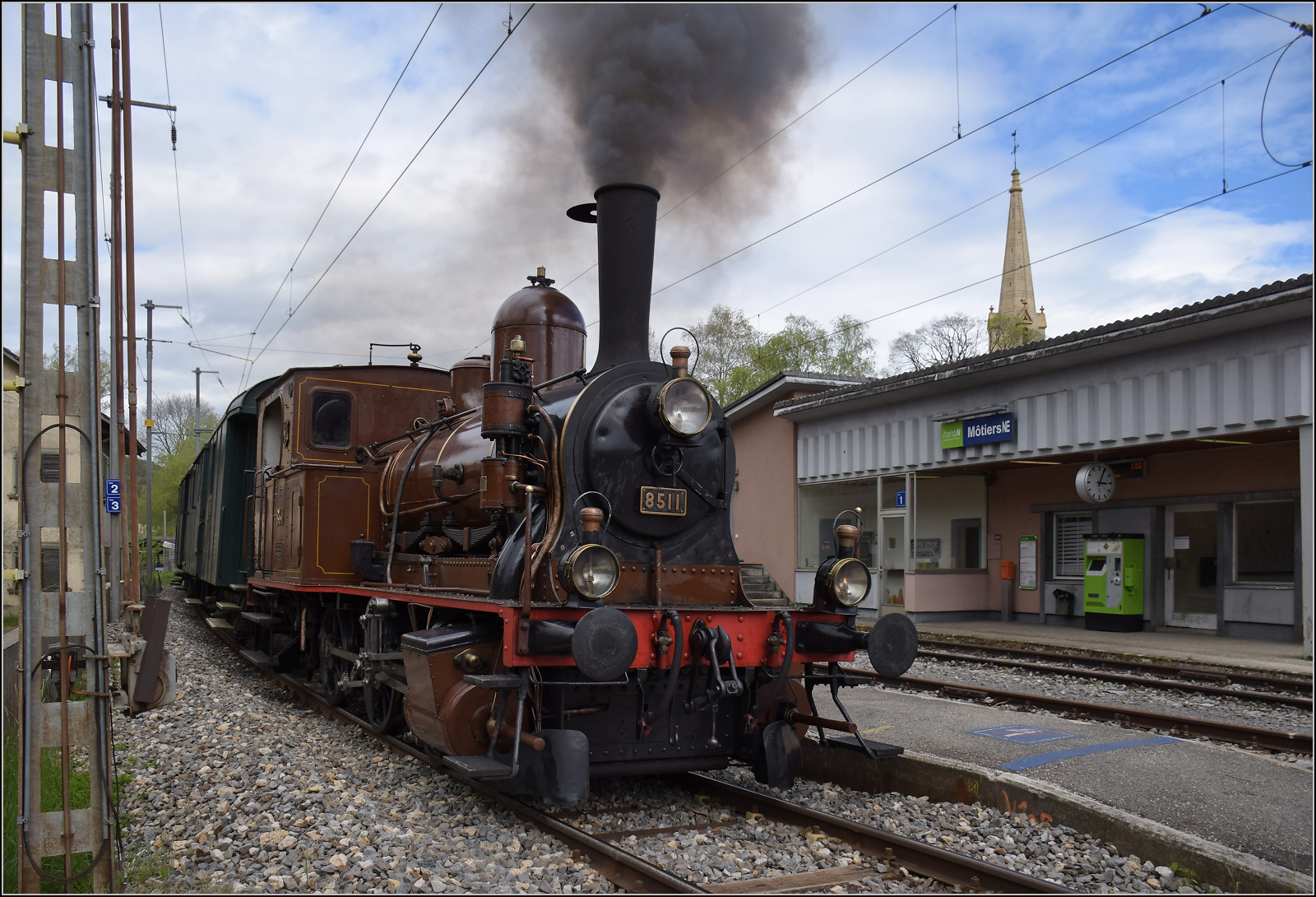 Train au fil de l'Areuse.

E 3/3 5811 in Môtiers. Das historisch bedeutsame Münster ist leider kaum in ein Foto zu integrieren. Lediglich die Kirchturmspitze ragt ins Bild. Angesichts des bevorstehenden Streckenumbaus darf bei diesen Bildern der Dampfzug die Nebensache sein. Mai 2024.