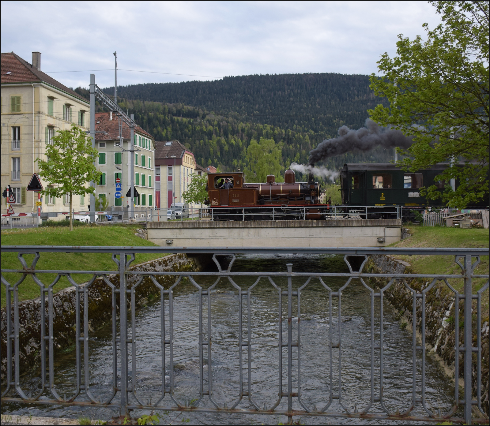 Train du Terroir.

E 3/3 5811 überquert die Buttes in Fleurier, dies ist der kleinere aber deutlich längere Nebenfluss der Areuse. Mai 2024.