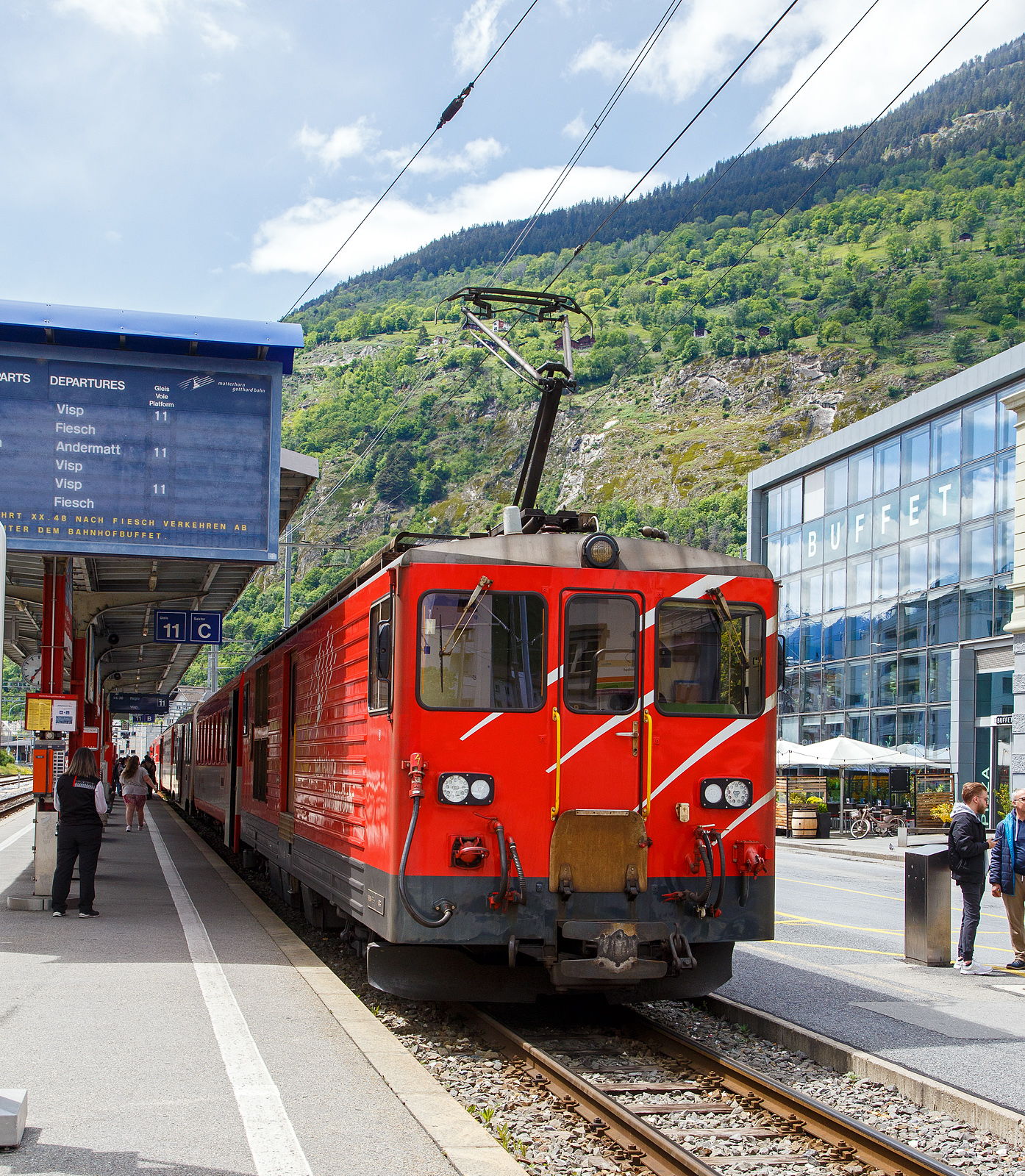 Von dem Gepäcktriebwagen Deh 4/4 II - 96  Münster   der Matterhorn-Gotthard-Bahn (MGB), ex FO 96  Münster   (Furka-Oberalp-Bahn), geschoben erreicht am 25.05.2023 der Regionalzug von Andermatt nach Visp den Bahnhof (Vorplatz) Brig.

Der Gepäcktriebwagen wurde 1984 von SLM (mechanischer Teil, Lokomotivkasten) und BBC (elektrische Ausrüstung) gebaut.